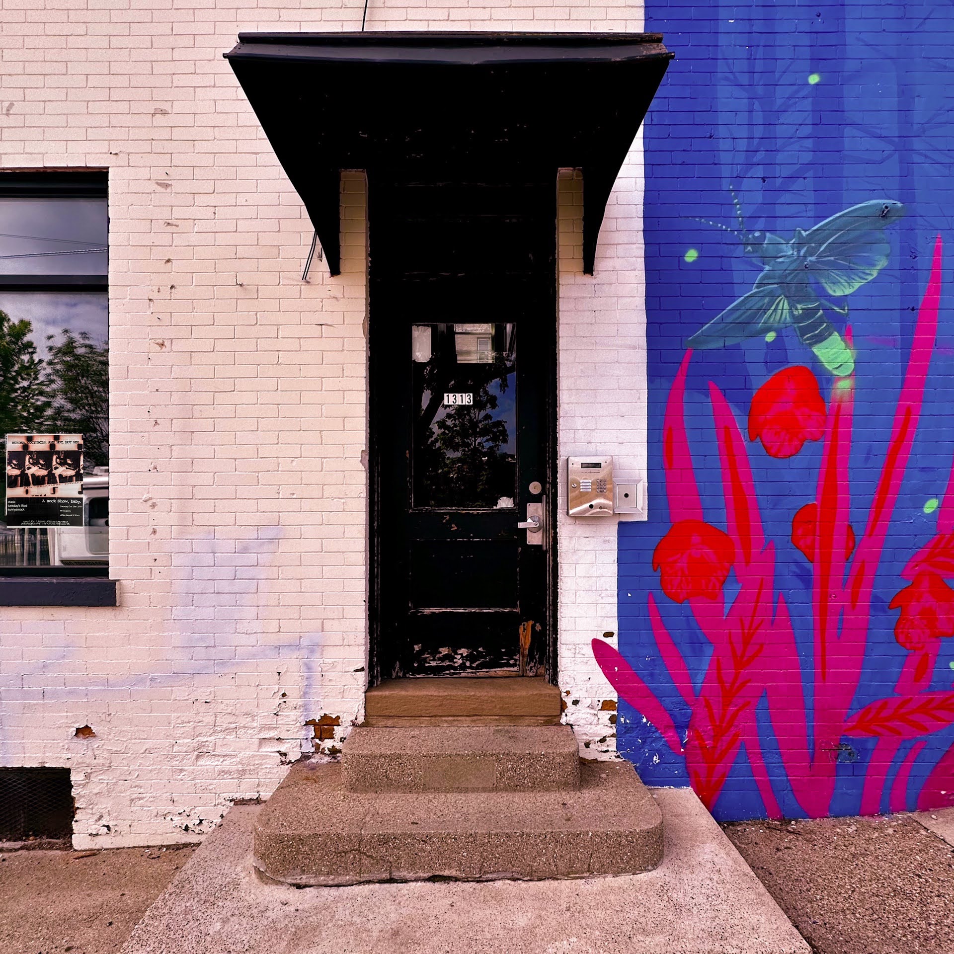 Original Sunnysmack 1313 artwork: the black door and awning, white brick, and blue wall with a pink flower mural